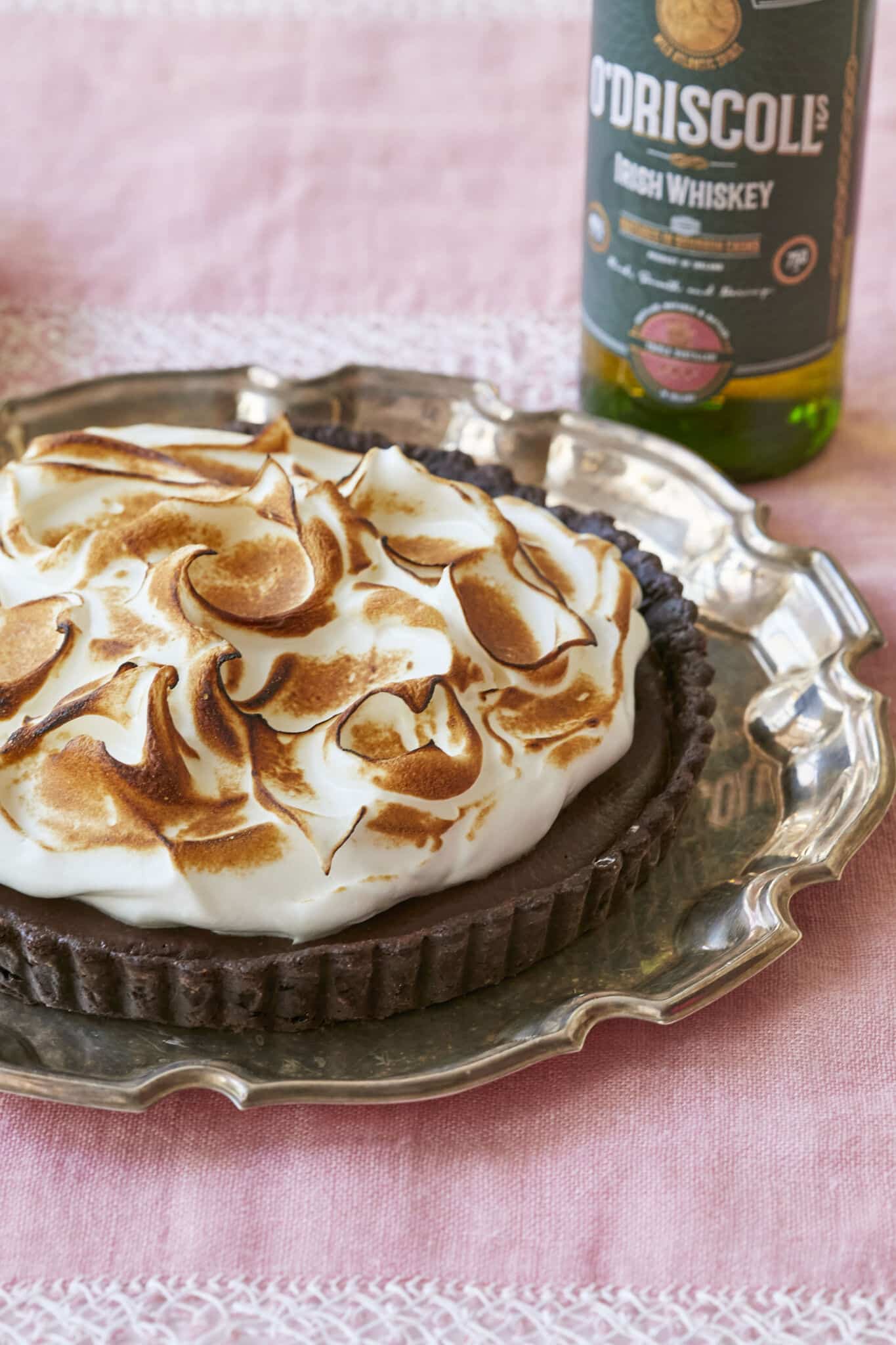 Irresistible Whiskey Chocolate Meringue Tart is served on a silver platter. It has decadent chocolate crust, rich and smooth chocolate filling, topped with velvety toasted meringue. 