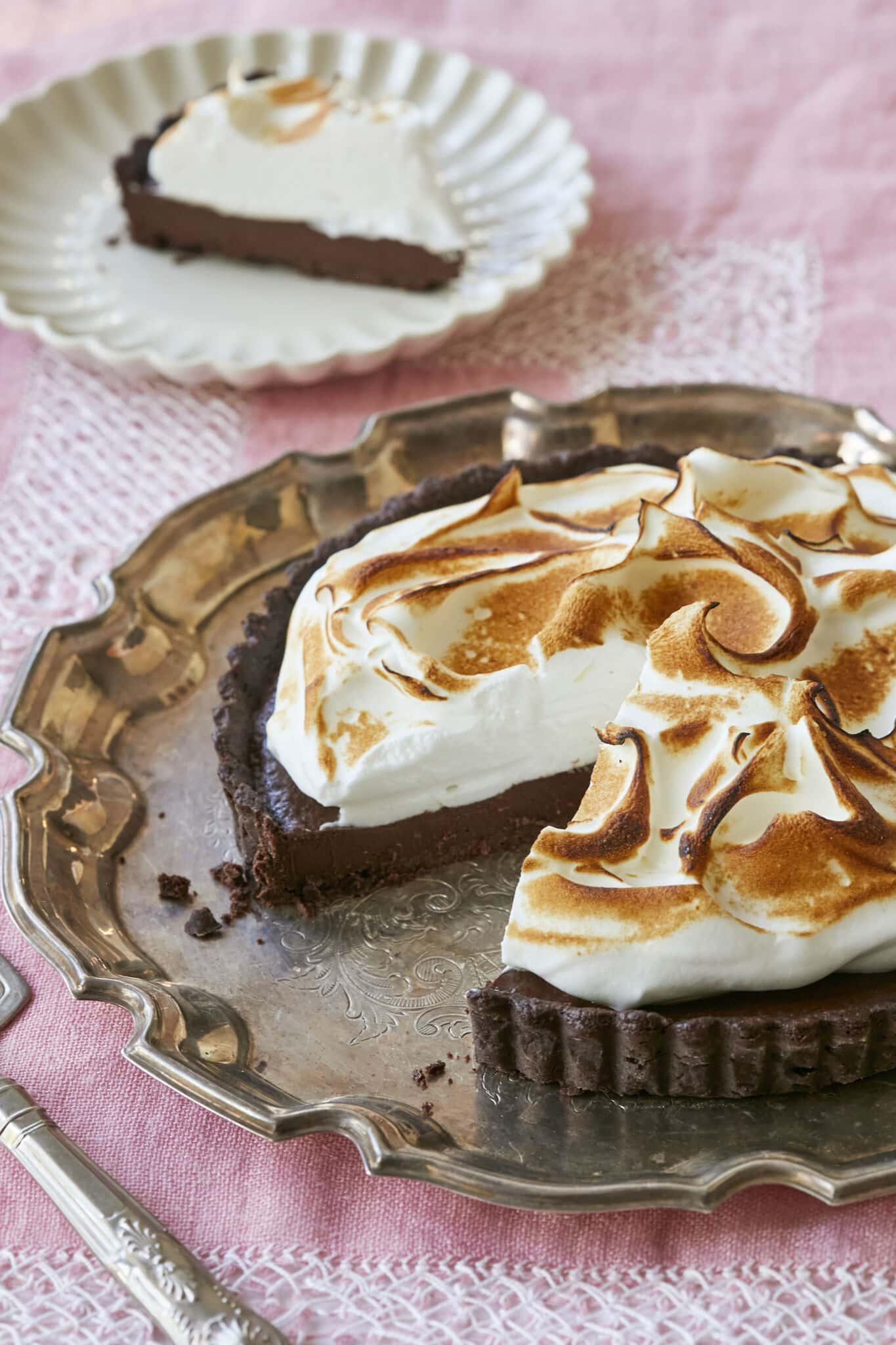 Irresistible Whiskey Chocolate Meringue Tart is served on a silver platter. It has decadent chocolate crust, rich and smooth chocolate filling, topped with velvety toasted meringue. A slice is cut and slice is cut and served on a white dresser plate. 