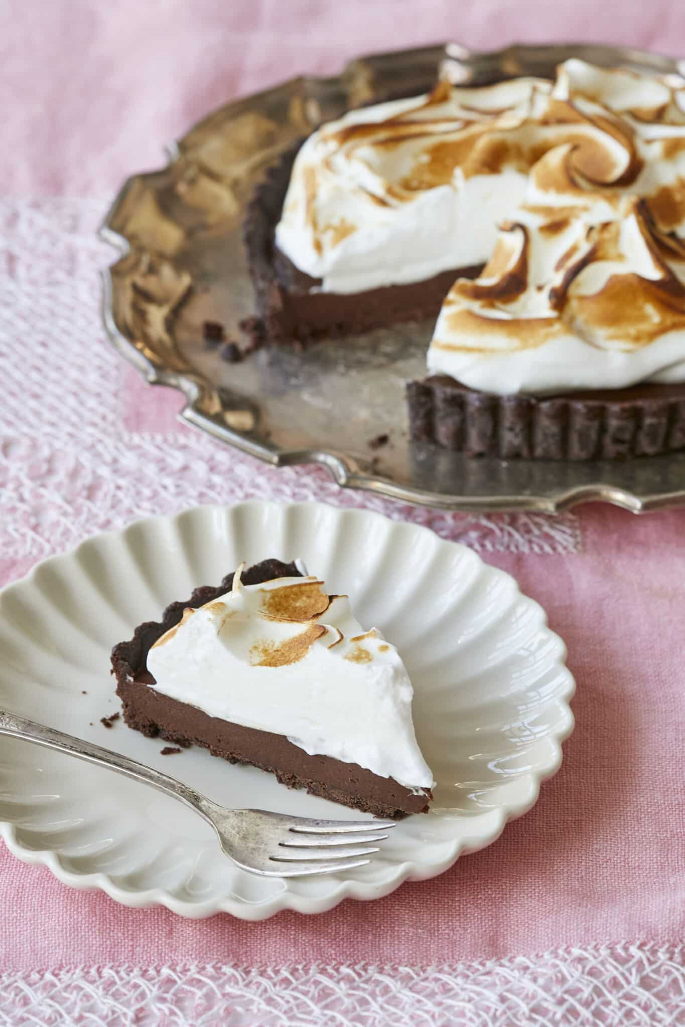 Irresistible Whiskey Chocolate Meringue Tart is on a silver platter and a slice has been cut and is served on a white dessert plate. It has decadent chocolate crust, rich and smooth chocolate filling, topped with velvety toasted meringue. 
