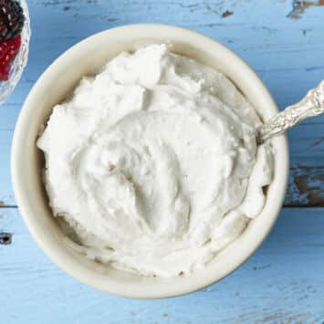 A bowl of thick, creamy coconut whipped cream with a bowl of mixed berries on the side.