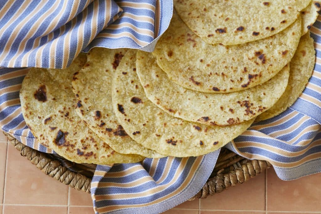 A stack of Homemade Corn Tortillas are golden and bubbly on top.