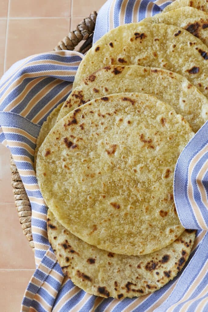 A stack of Homemade Corn Tortillas are golden and bubbly on top.