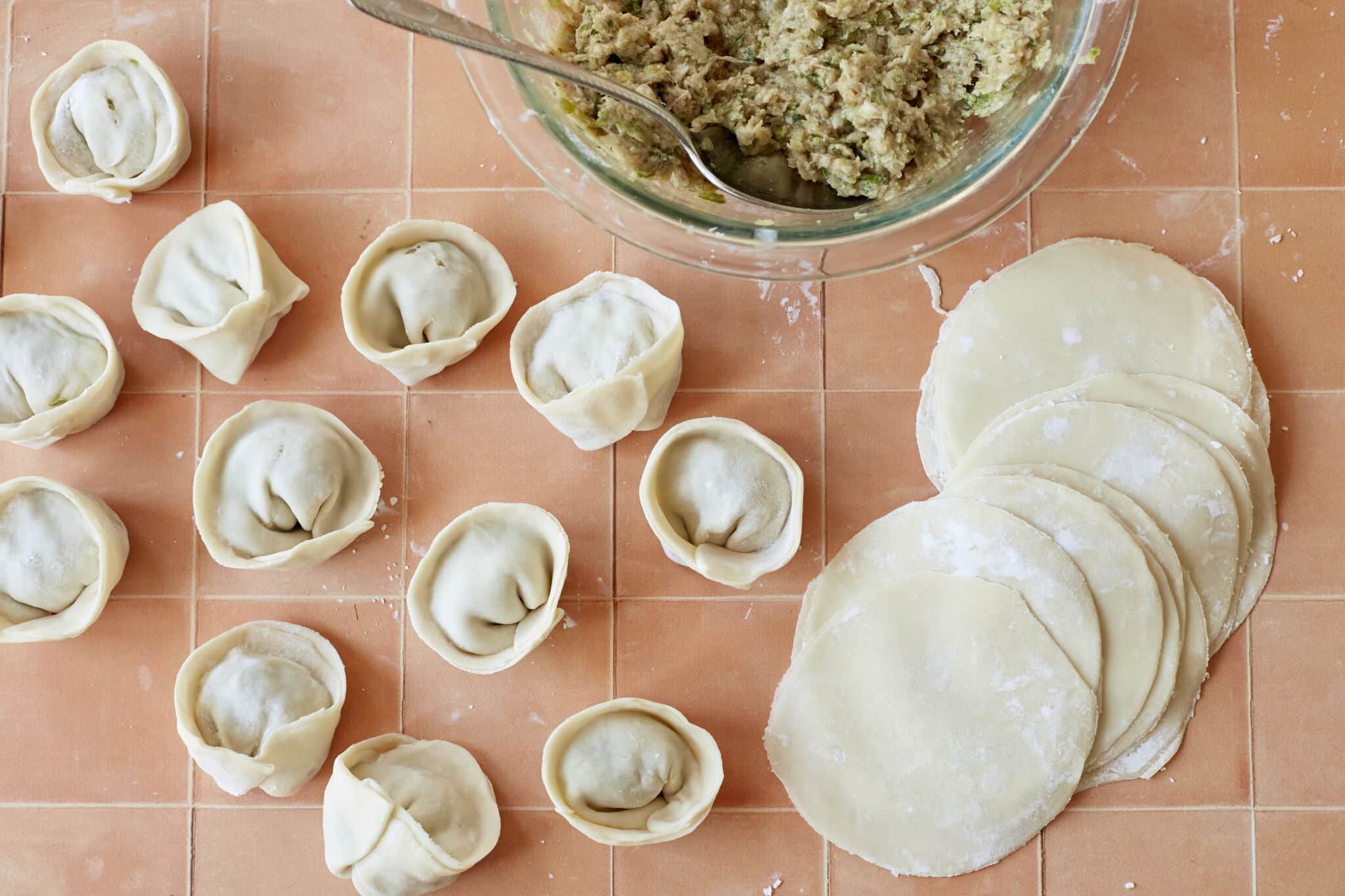 Thin, delicate Homemade Dumpling Wrappers with some dumplings. A bowl of filling is on the side.