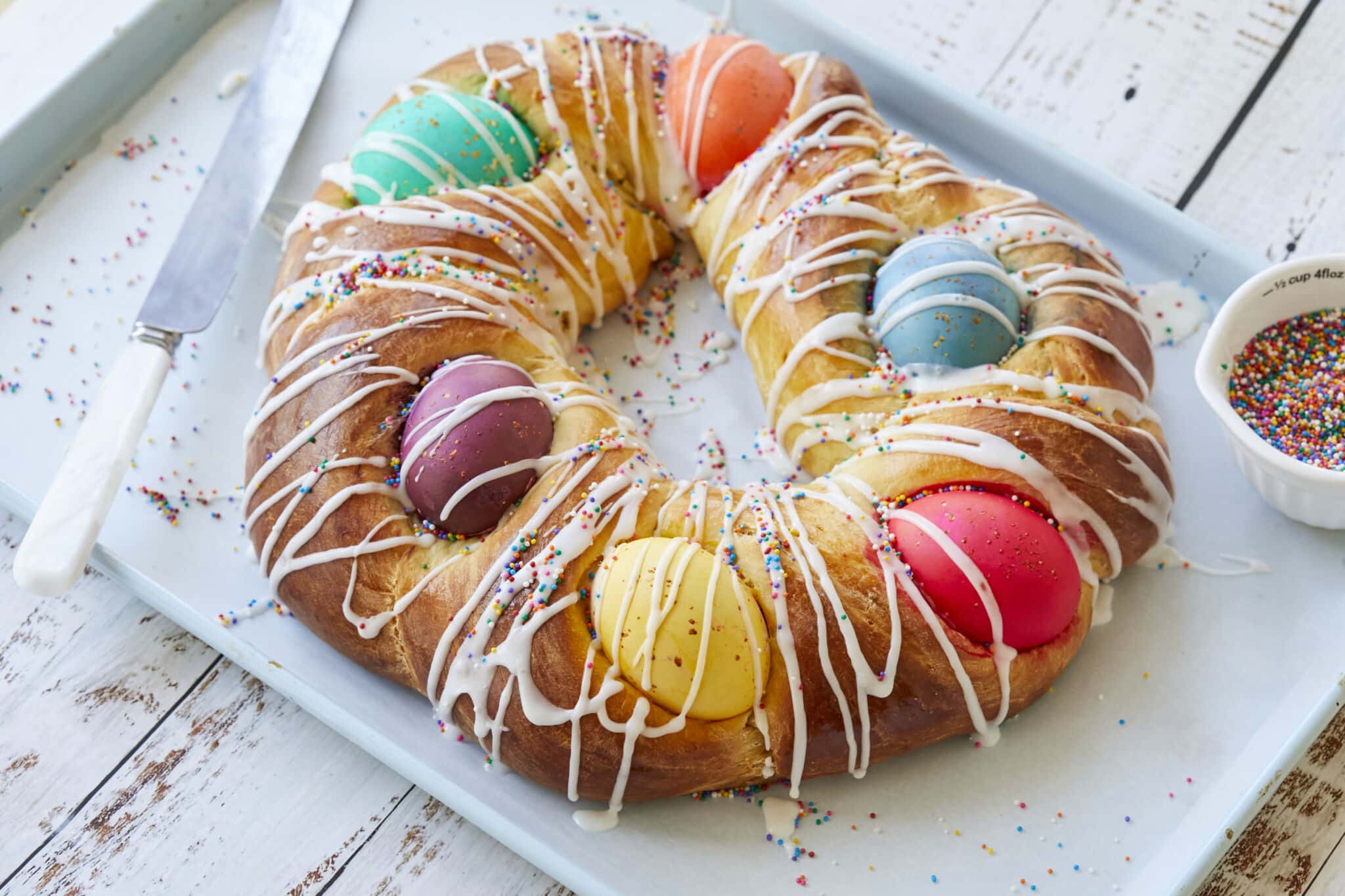 Traditional Italian Easter Bread (Pane di Pasqua) is golden, light and fluffy, and decorated with colorful Easter eggs, drizzled with icing and topped with colorful sprinkles.