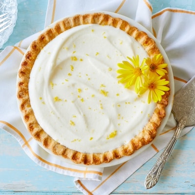 An over-head shot shows that the Luscious Creamy Lemon Chiffon Pie has a golden curst with a white, silky filling, topped with refreshing lemon zest and two flowers.