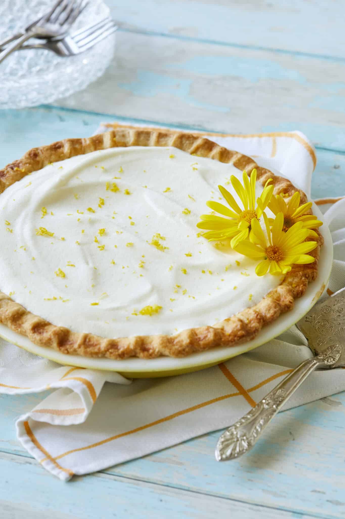 Luscious Creamy Lemon Chiffon Pie has a golden curst with a white, silky filling, topped with refreshing lemon zest and two flowers. 