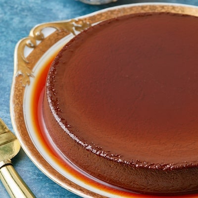 Mexican Chocolate Flan is served on a golden rim platter. The flan is silky smooth in deep chocolate color and covered with a thin layer of caramel.