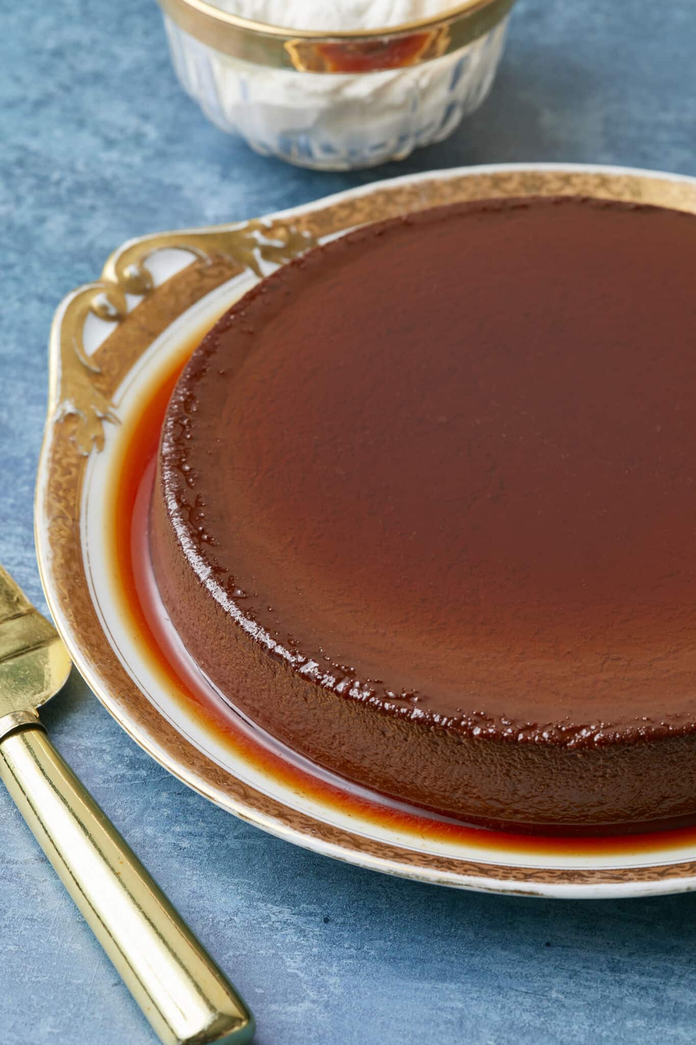 Mexican Chocolate Flan is served on a golden rim platter. The close-up shot shows that it is silky smooth in deep chocolate color and covered with a thin layer of caramel. 