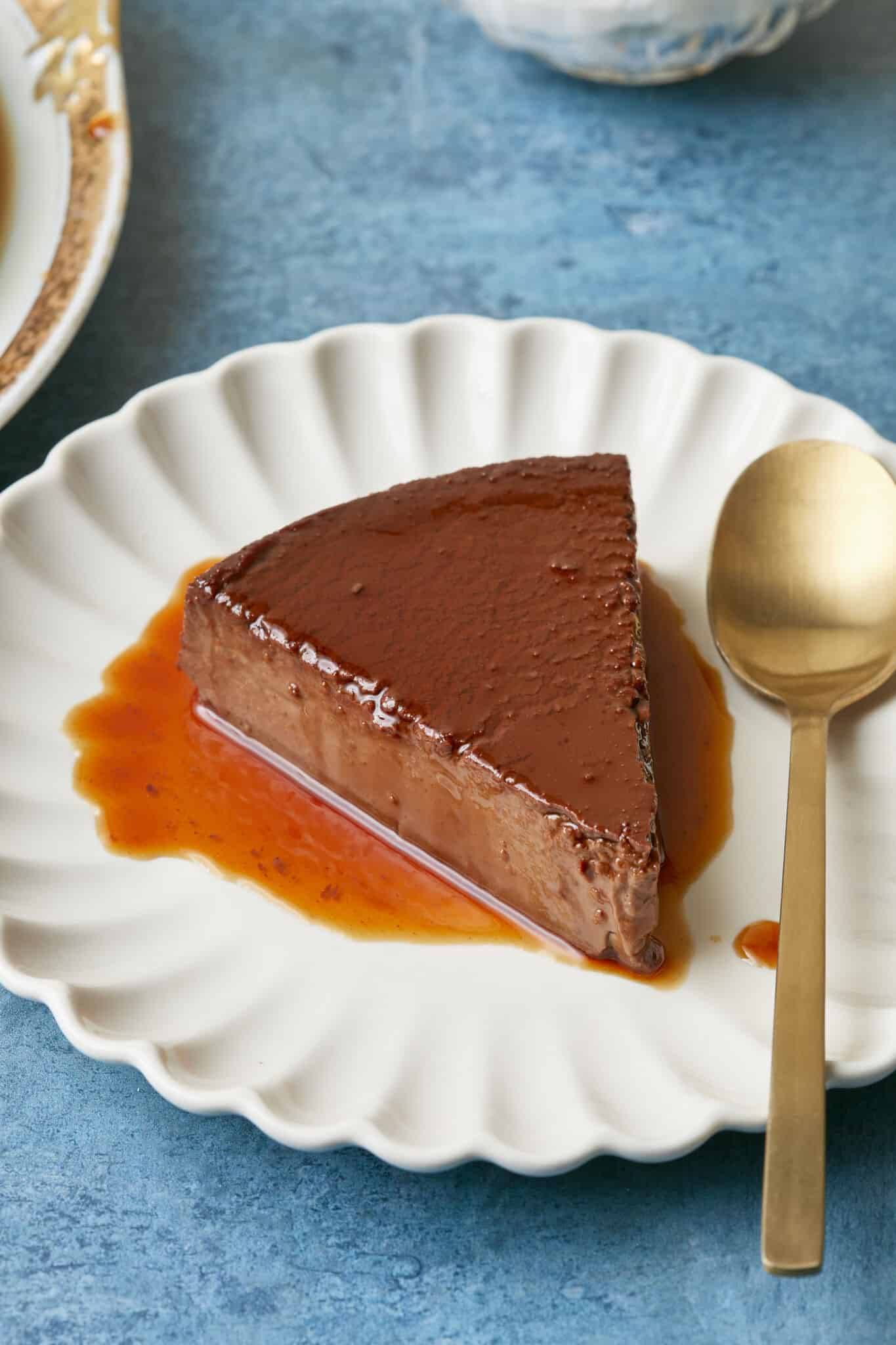A slice of Mexican Chocolate Flan is served on a white dessert plate. It is silky smooth in deep chocolate color and covered with a thin layer of caramel. 