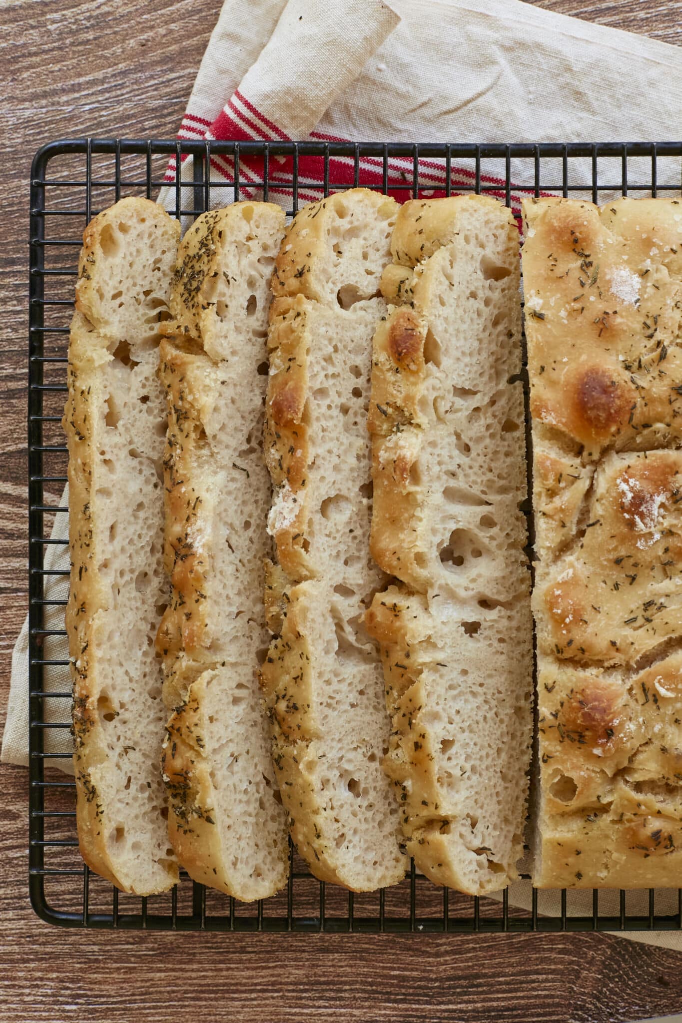 No-knead focaccia is sliced and cooling on the black wire rack. The close-up shot shows it bubbly crumb and golden, crispy exterior. 