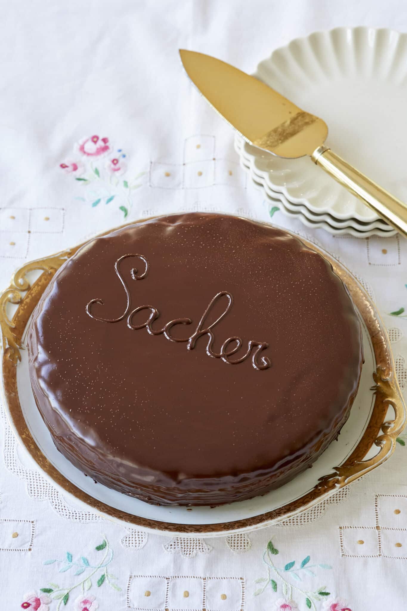 Classic Austrian Sacher Torte is placed on a round golden rim platter. It shows the silky smooth, shinny glaze. 
