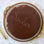 Classic Austrian Sacher Torte is placed on a round golden rim platter. It shows the silky smooth, shinny glaze.