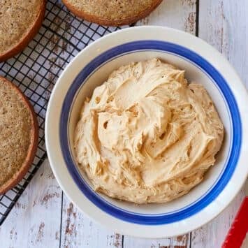 A big bowl of smooth Salted Caramel Buttercream Frosting is next to three round cake layers.