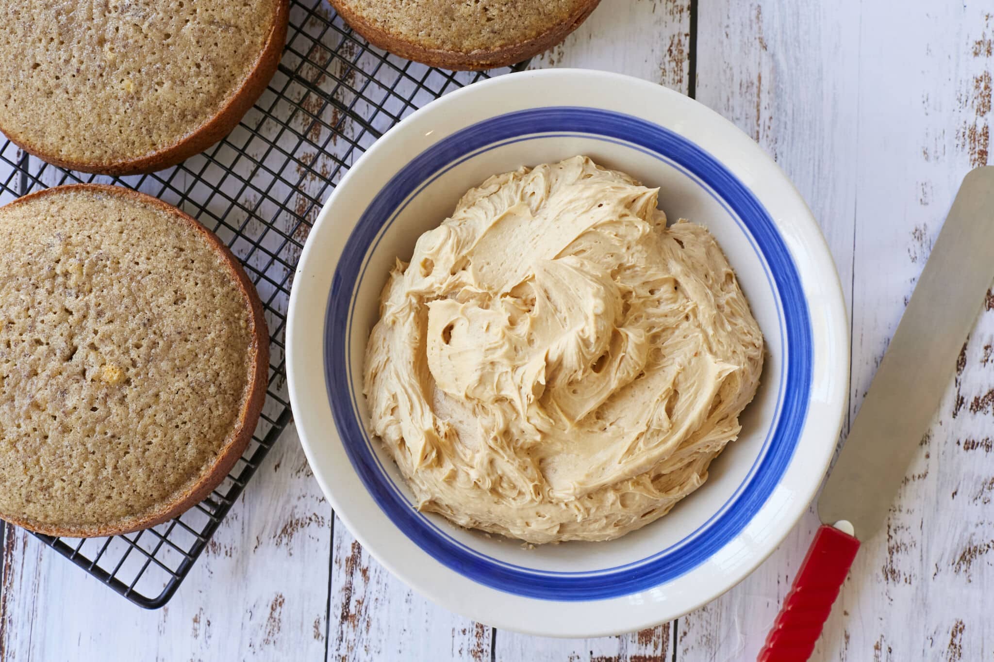 A big bowl of smooth Salted Caramel Buttercream Frosting is next to three round cake layers.