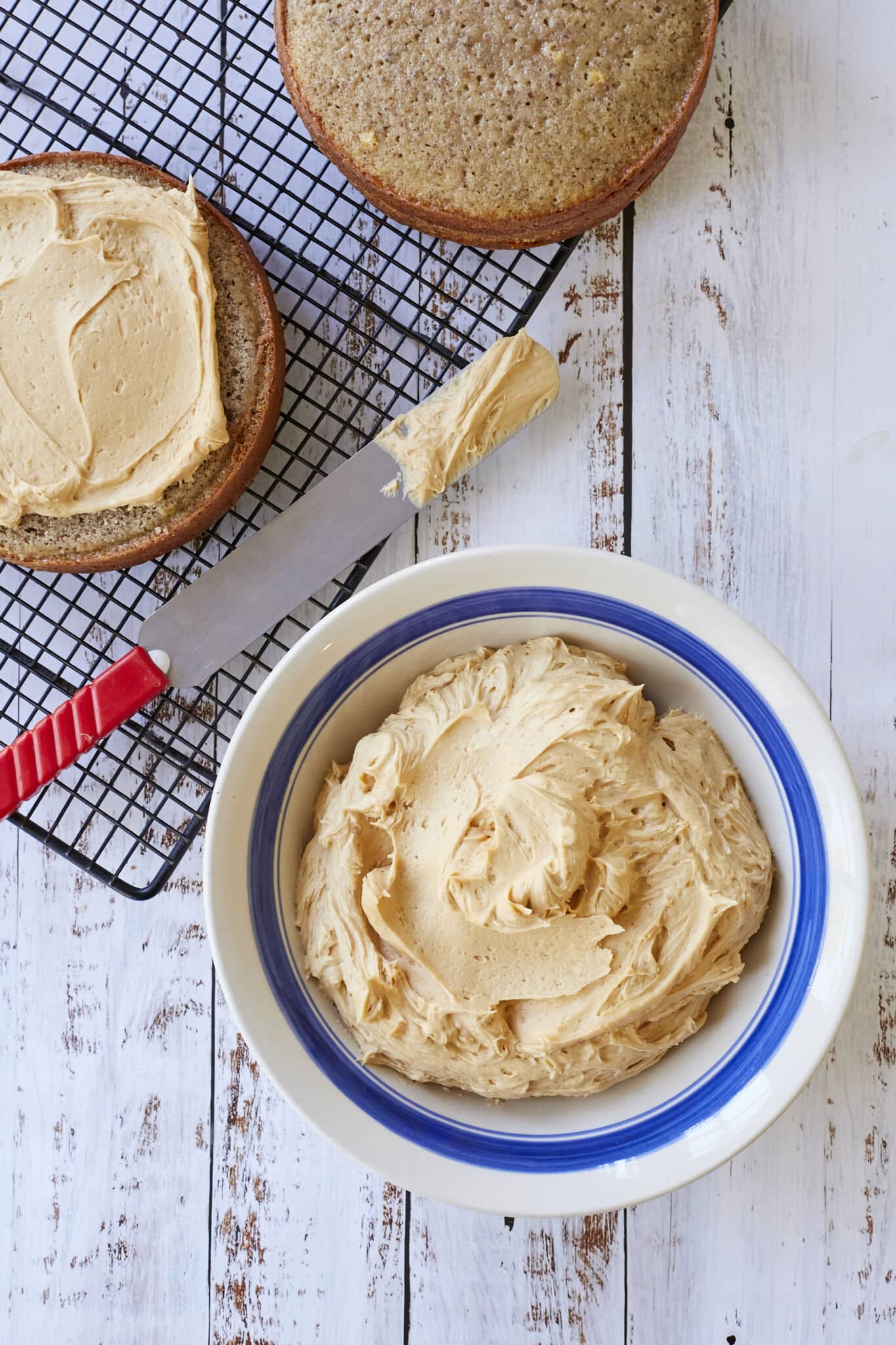 A big bowl of smooth Salted Caramel Buttercream Frosting is next to two round cake layers. One has been frosted.