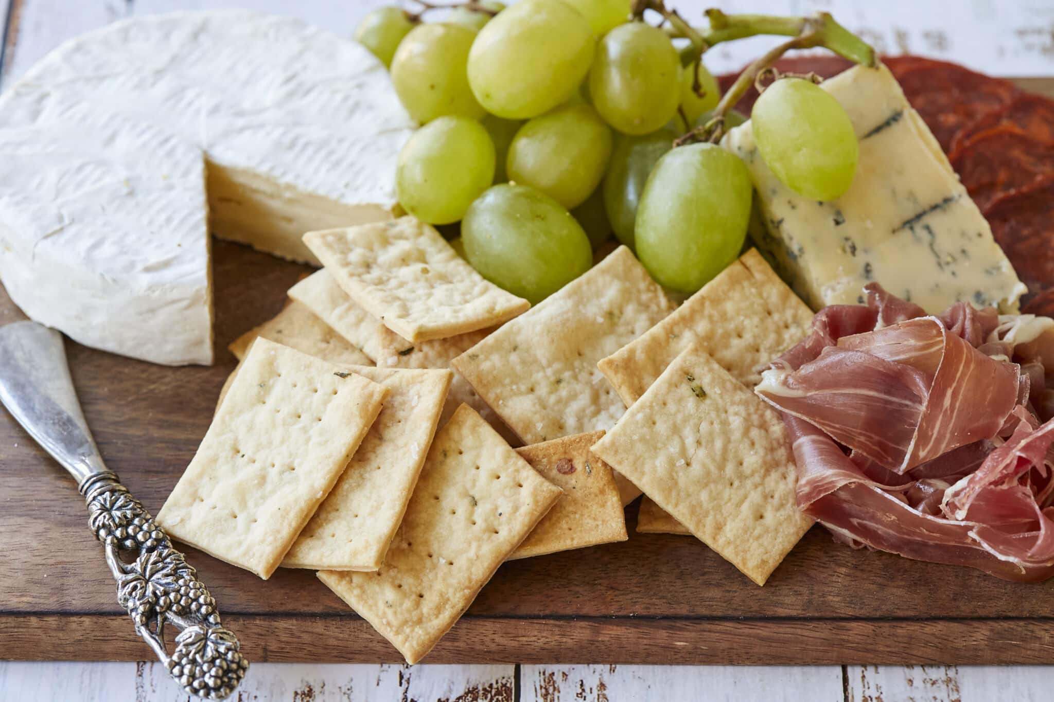 Homemade Sourdough Crackers are served on a charcuterie board with green grapes, prosciutto, cheese and salami.