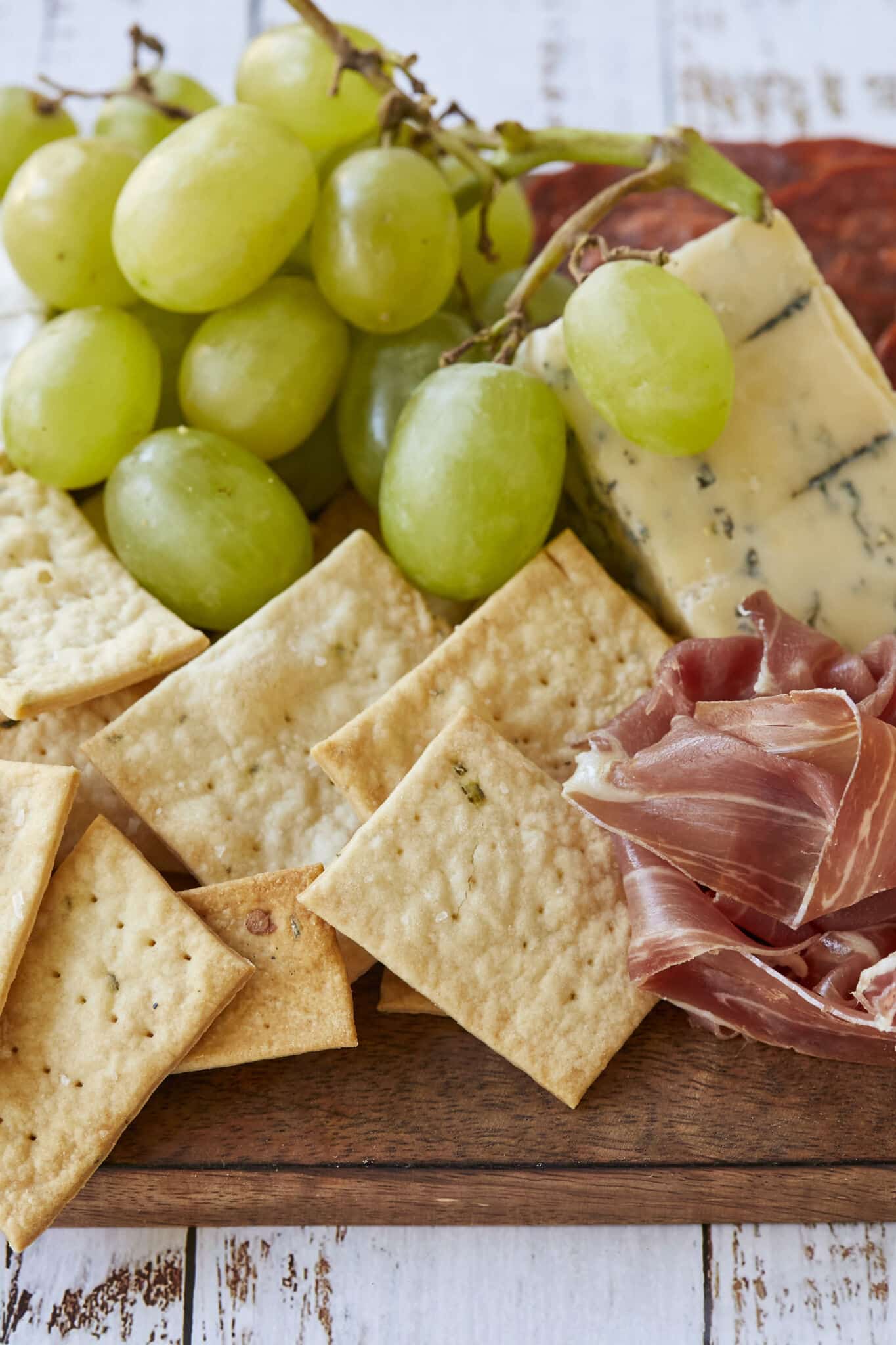 Homemade Sourdough Crackers are served on a charcuterie board with green grapes, prosciutto, cheese and salami.