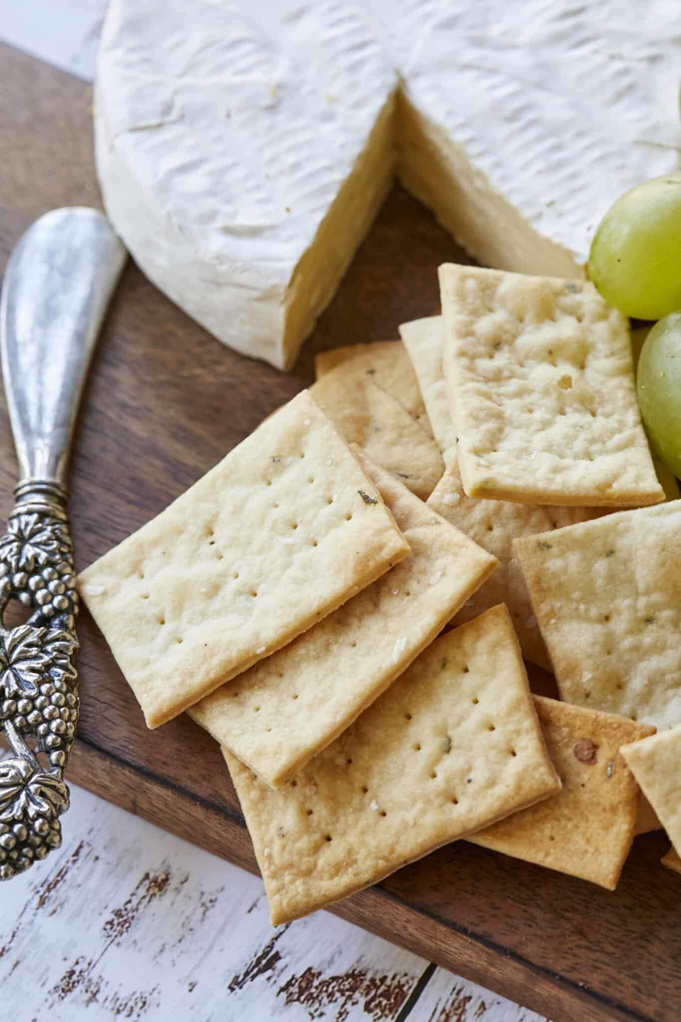Homemade Sourdough Crackers are served on a charcuterie board with green grapes and cheese. 