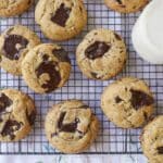 Sourdough Chocolate Chip cookies are baked golden brown with pools of chocolate throughout are cooling on a wire rack. They're paired with milk.