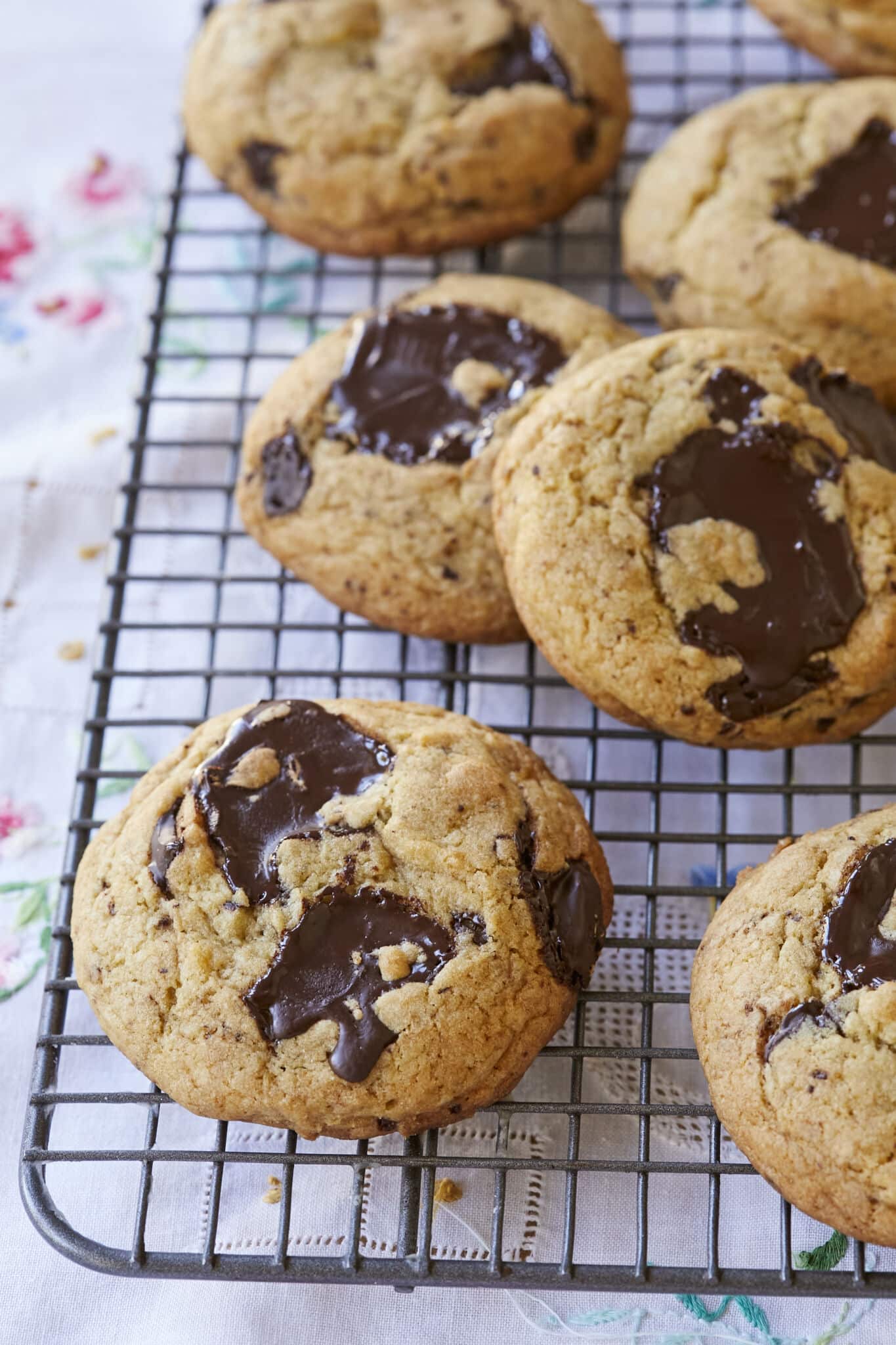 The close-up shows that Sourdough Chocolate Chip cookies are baked golden brown with pools of chocolate throughout are cooling on a wire rack.