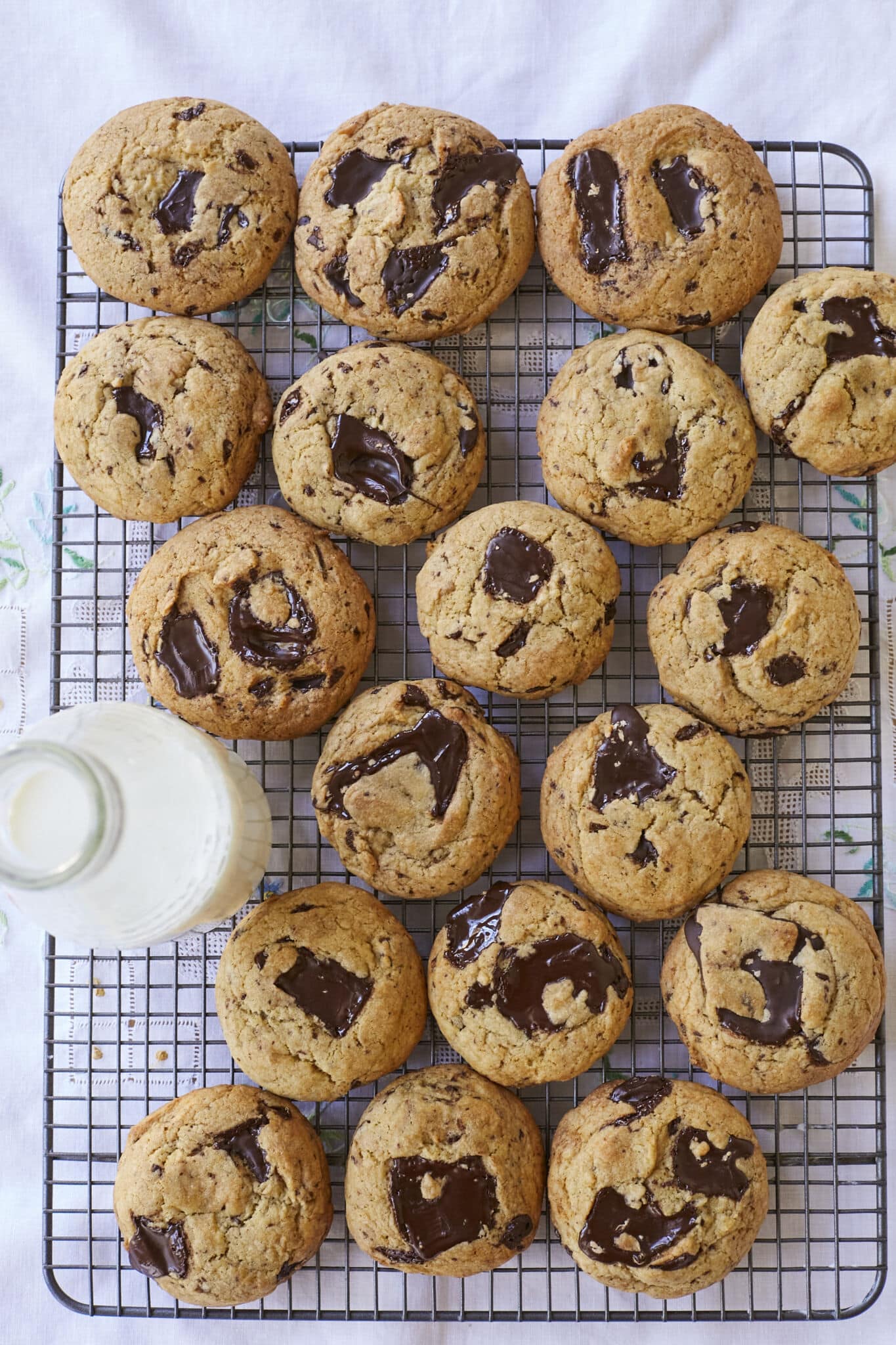 Sourdough Chocolate Chip cookies are baked golden brown with pools of chocolate throughout are cooling on a wire rack. They're paired with milk.