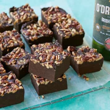 A close shot at squares of the fudge, showing its soft fudgy texture, with a bottle of Irish Whiskey in the back.
