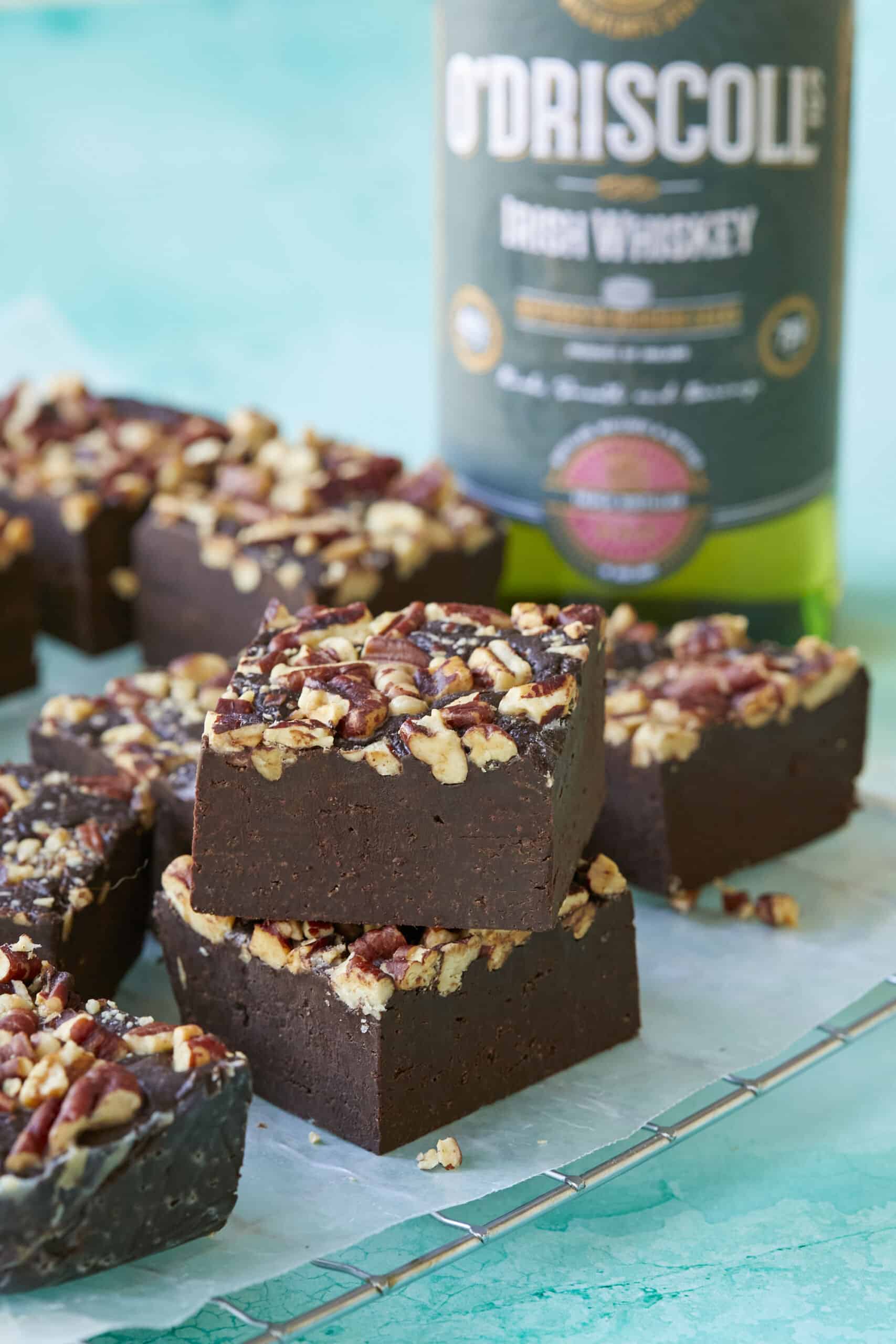 A close shot at squares of the fudge, showing its soft fudgy texture, with a bottle of Irish Whiskey in the back. 