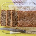 A loaf of golden, moist, soft Almond Banana Bread is sliced and cooling on the wire rack.