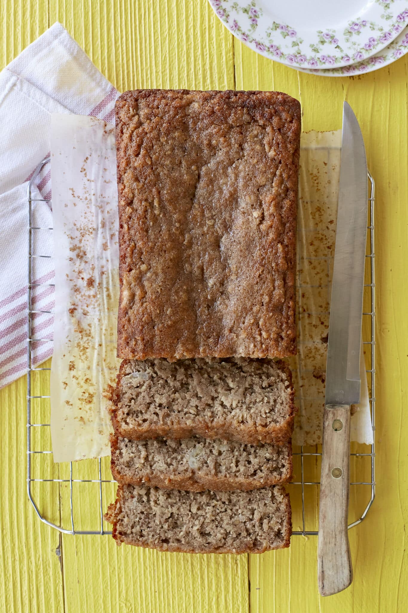 A loaf of golden, moist, soft Almond Banana Bread is sliced and cooling on the wire rack. 