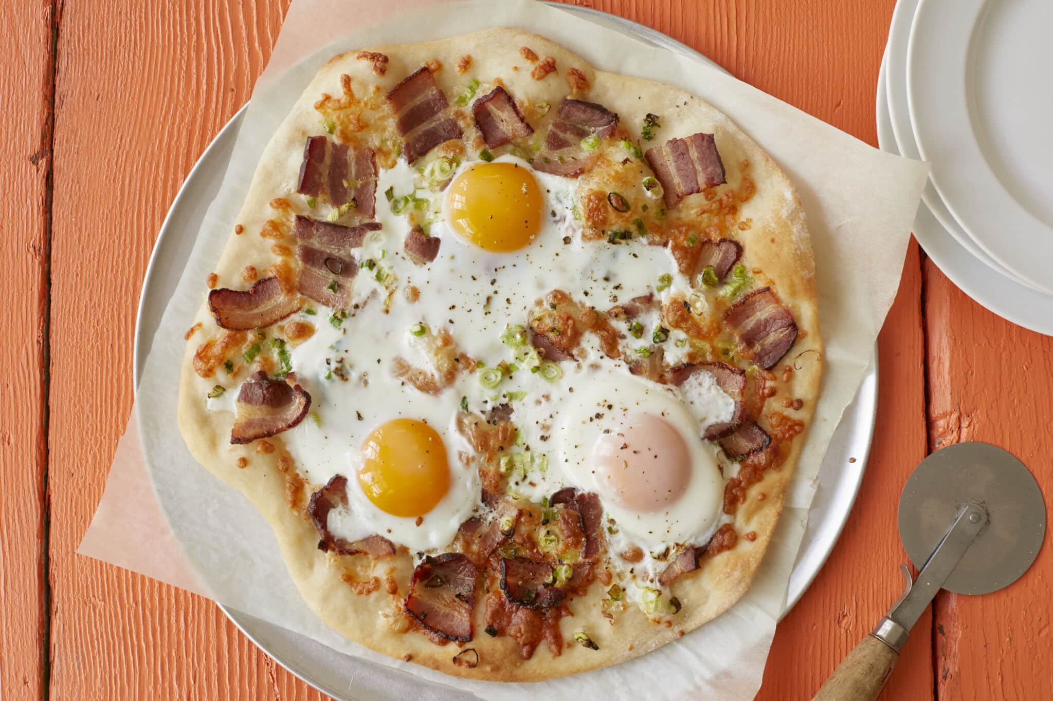 Wholesome breakfast pizza has golden and crispy crust, with smoky bacon, green onions, and sunny-side-up eggs bringing layers of savory flavor.
