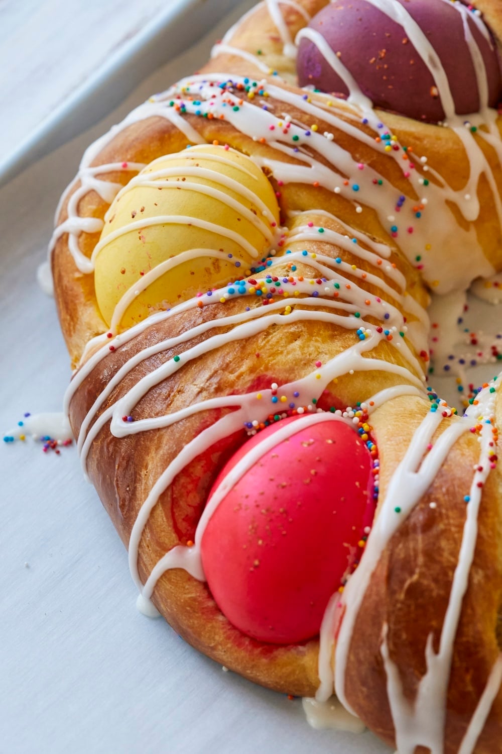 A close-up shot at the edge of the golden brown Italian Easter Bread with a yellow and a red egg. 
