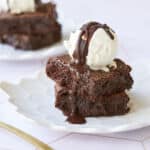 A close-up shot at Gluten-Free Almond Flour Brownies shows the fudge inside and chunks of chocolate with shinny, crinkly top. They're served with ice cream and chocolate sauce.