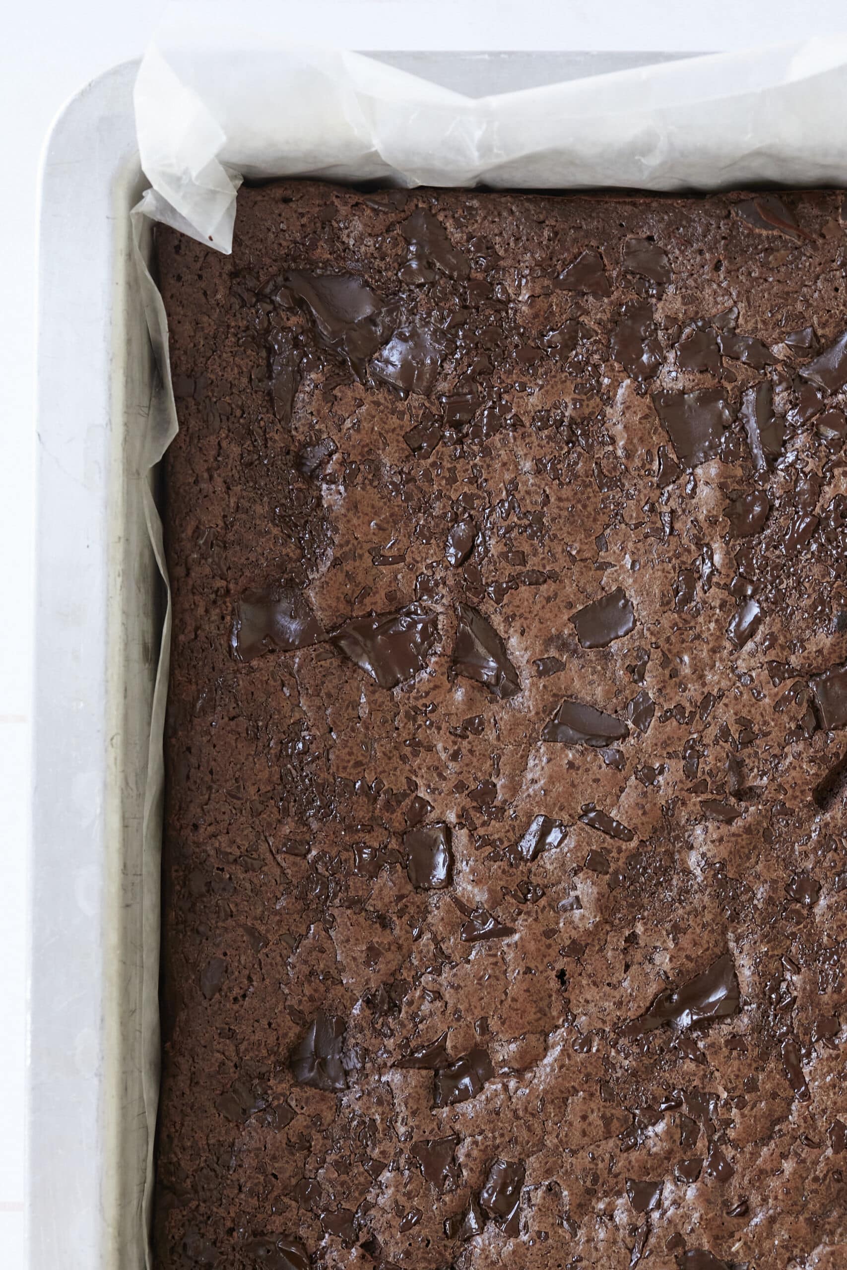 Gluten-Free Almond Flour Brownies are baked in parchment paper, loaded with chunks of chocolate, and have shinny, crinkly top. 