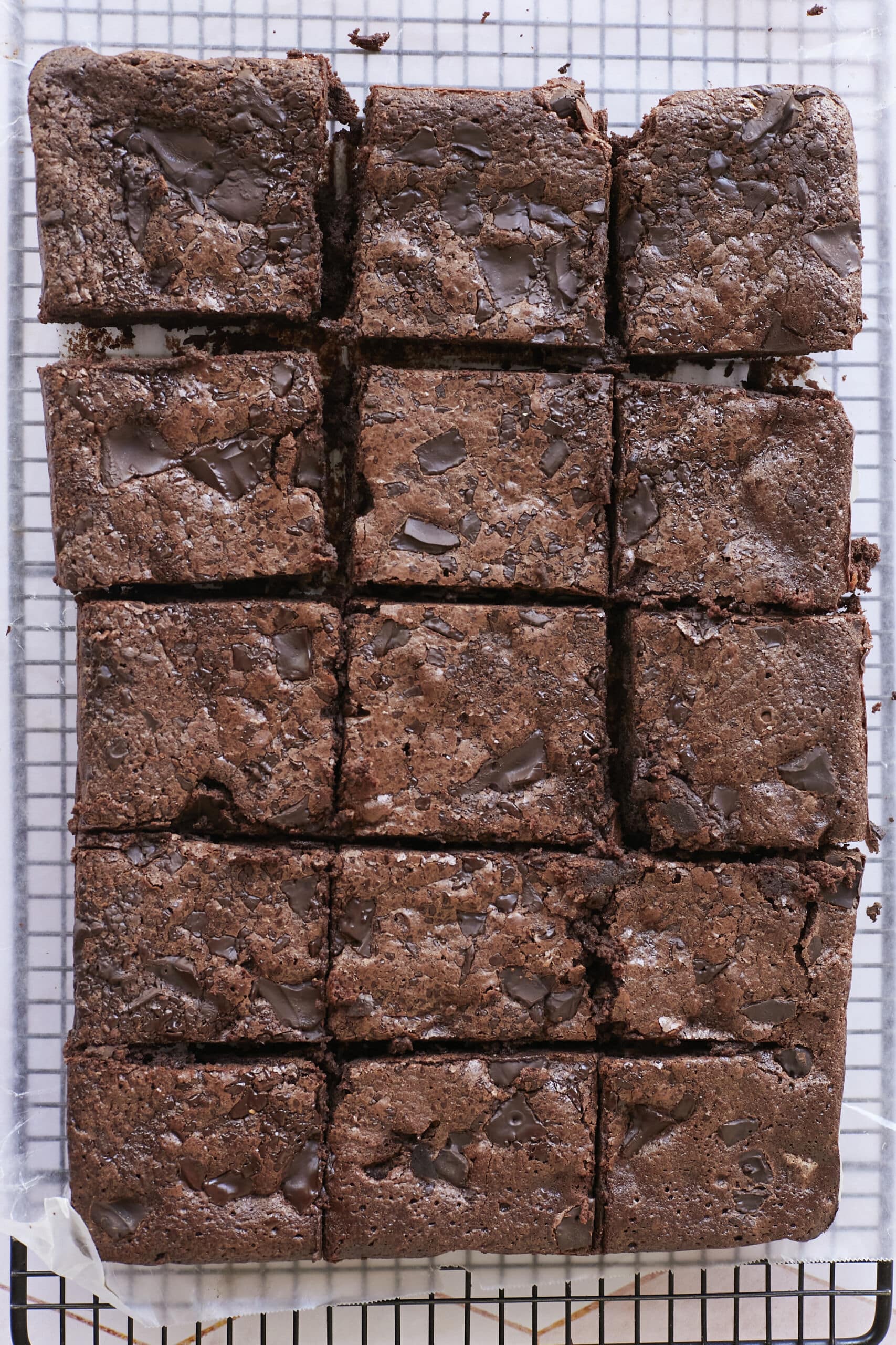 Gluten-Free Almond Flour Brownies are cut into 15b big squares, cooling on the wire rack. They're loaded with chunks of chocolate and have shinny, crinkly top. 