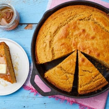 the cornbread in a hot cast iron pan with a delectably crunchy and browned crust. A slice is served on a dessert plate with butter on top and extra honey in a jar on the side.