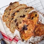 A top-down view of a loaf of golden brown Olive Bread on a cooling rack, shows its bubbly crumb and thick, crispy crust, loaded with fruit.