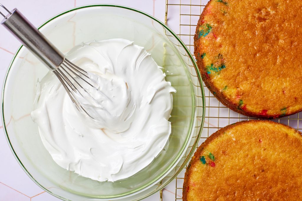 A bowl of meringue-like 7 Minute Frosting is served with two slices of cake loaded with sprinkles.