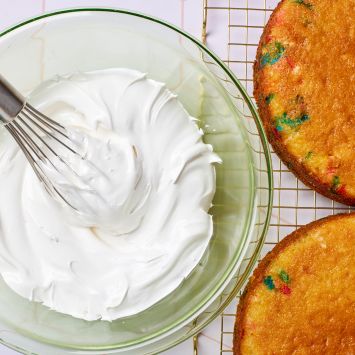 A bowl of meringue-like 7 Minute Frosting is served with two slices of cake loaded with sprinkles.