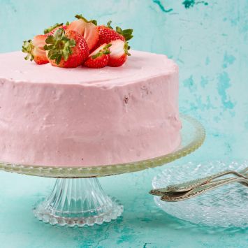 Fresh Strawberry Cake coated with light pink strawberry cream cheese frosting and topped with fresh strawberries.