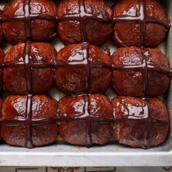 A top-down view of a tray of shiny fluffy Chocolate Hot Cross Buns.