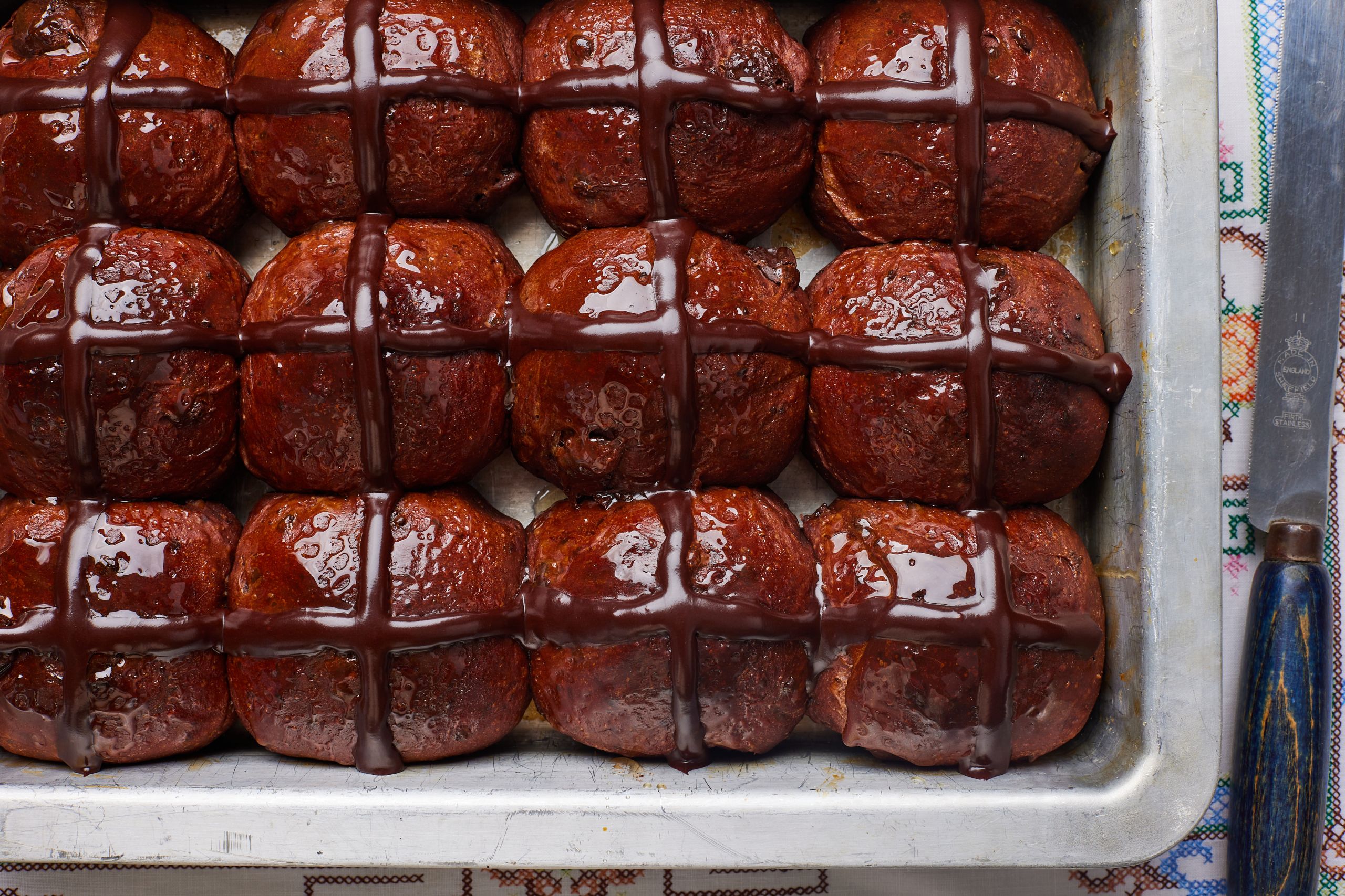 A top-down view of a tray of shiny fluffy Chocolate Hot Cross Buns.