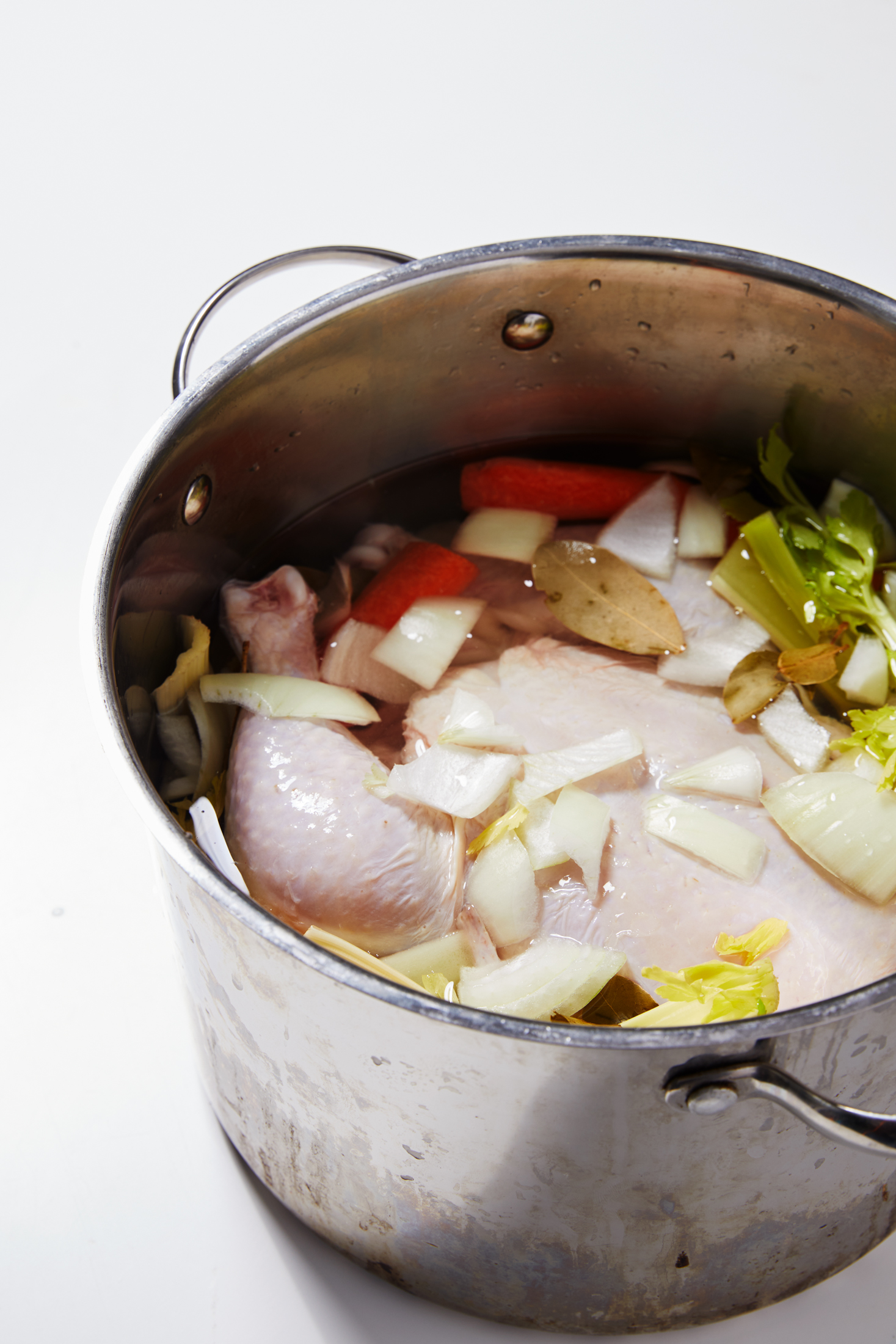 A pot of carrots, celery, onion, bay leaves, pepper and parsley with the whole chicken on top.