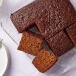 A molasses cake has been cut into 9 big squares on the cooling rack. Two are having the sides facing up, showing the moist and airy crumb. Whipped cream is served on the side.