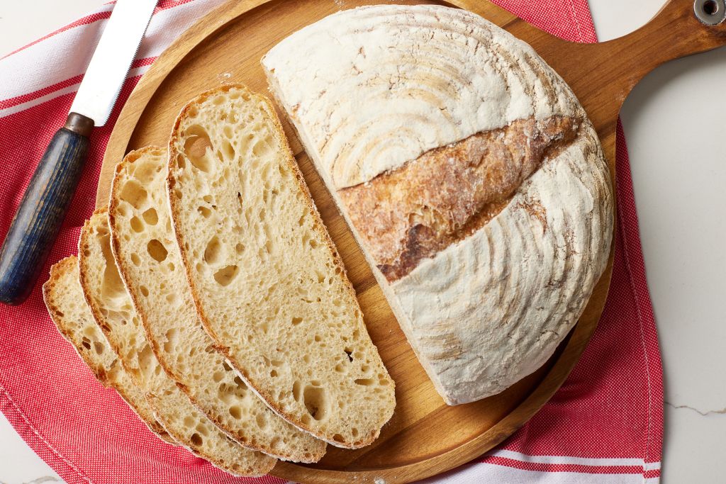 A top-down view of half loaf of bread with three slices on its left side shows the golden crust and bubbly, open crumb.