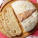 A top-down view of half loaf of bread with three slices on its left side shows the golden crust and bubbly, open crumb.