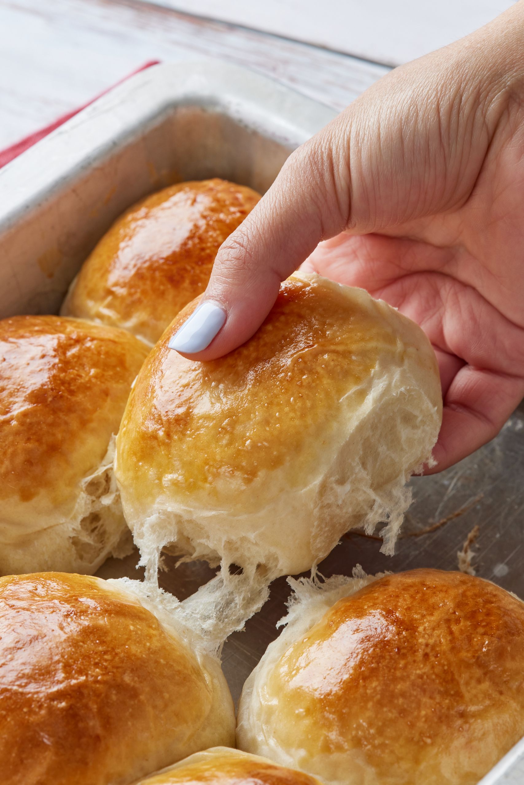 Soft, golden Sourdough Dinner Rolls are in the baking tray. One roll is being pulled away. 