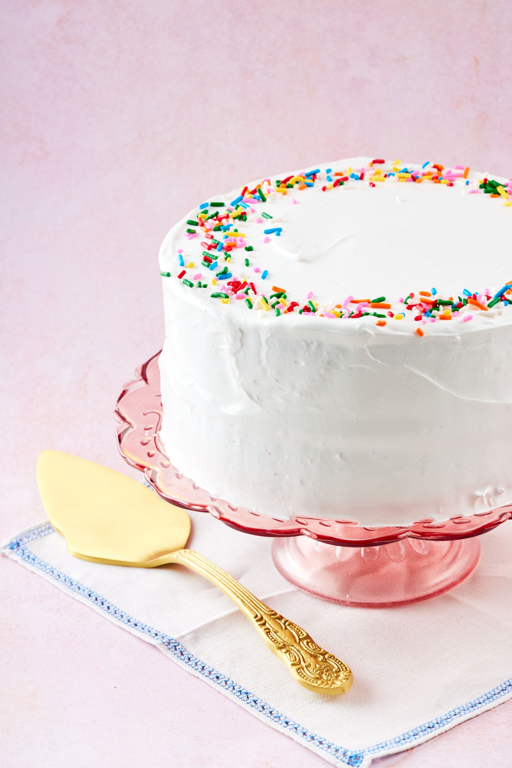 A $5 birthday cake is frosted with white frosting and topped with colorful sprinkles. 