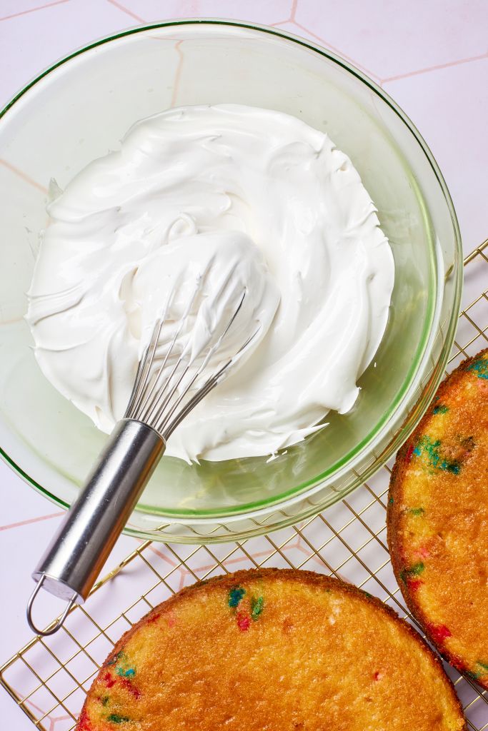 A bowl of meringue-like 7 Minute Frosting is ready for two slices of cake loaded with sprinkles.