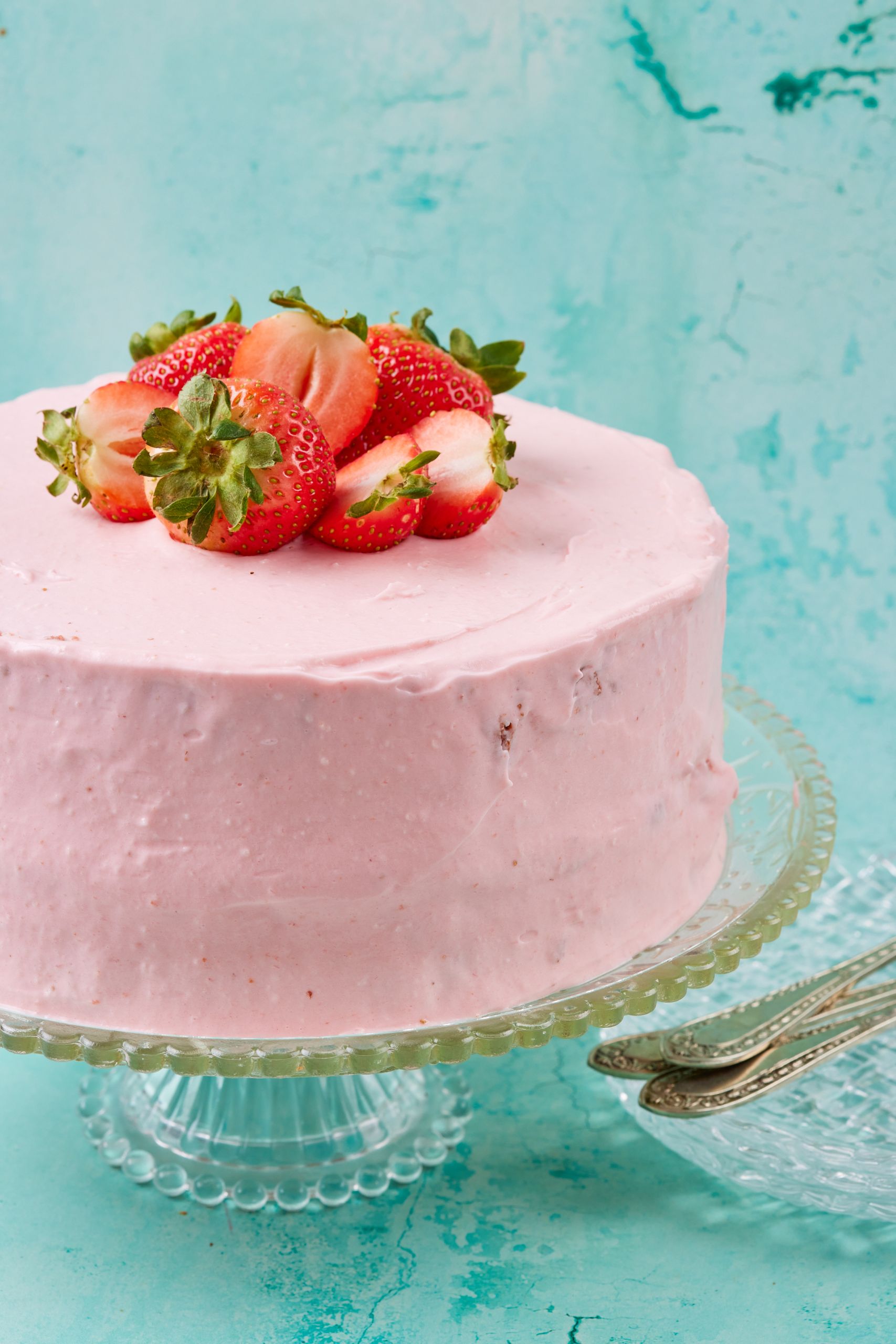 A close-up shot at a Fresh Strawberry Cake coated with light pink strawberry cream cheese frosting and topped with fresh strawberries. 