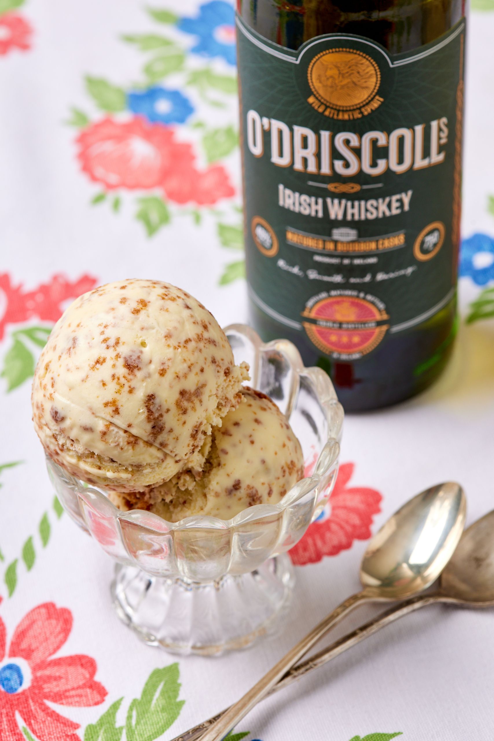 Two scoops of Brown Bread Ice Cream is served, with a bottle of Irish whiskey behind. 